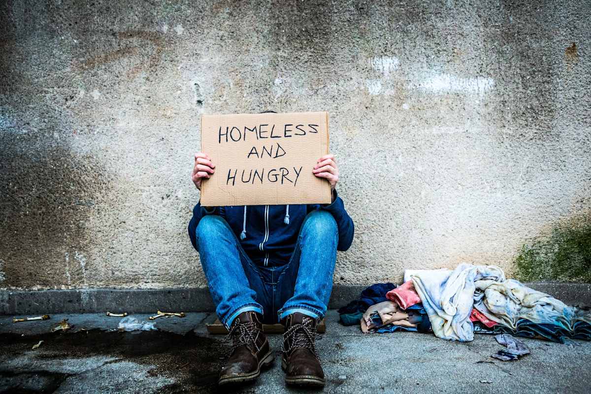 Man on the street holding a sign saying he is homeless and hungry.