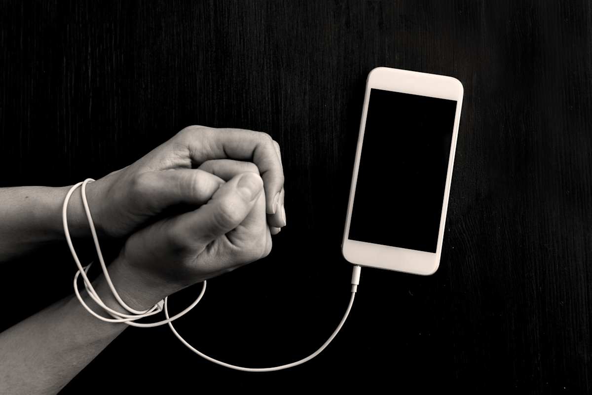 Hand and wrists wrapped with mobile phone cable attached to a phone.