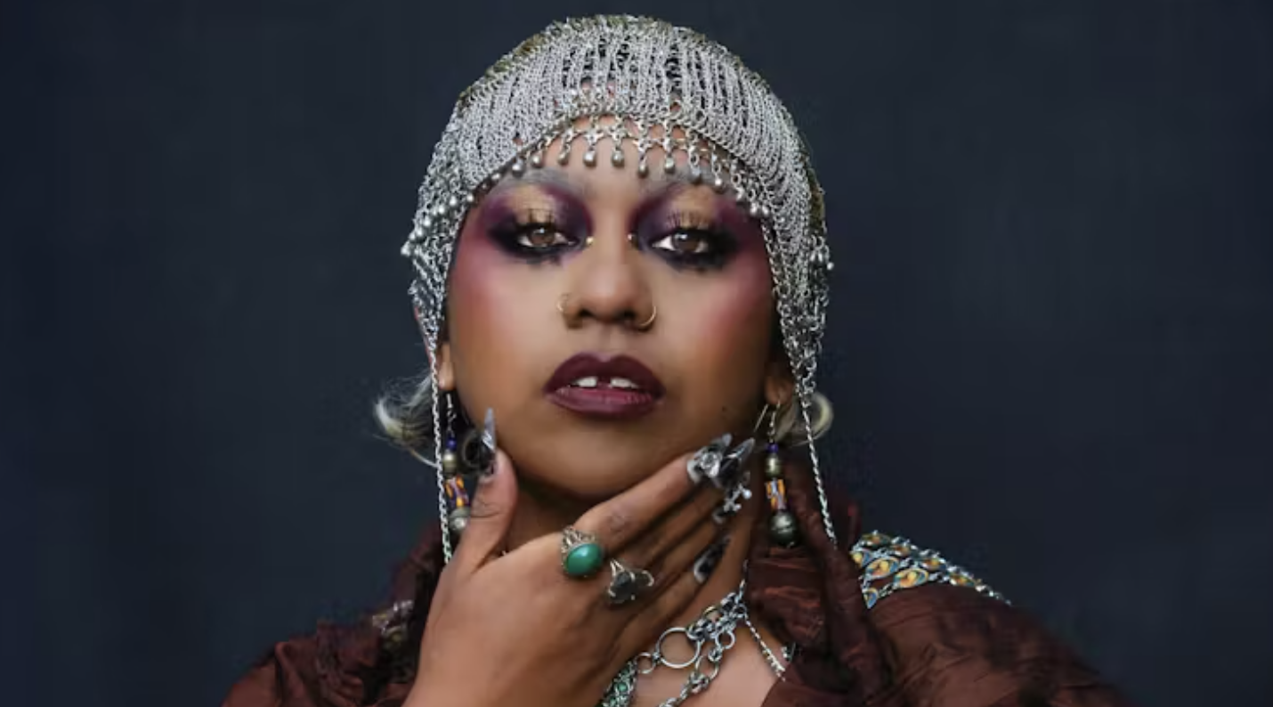 Portrat headshot of Emily Wurramara in a netallic headdress holding to hand to her chin
