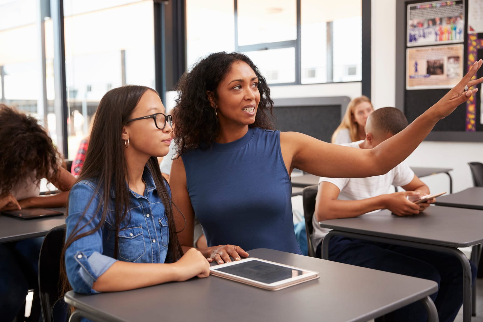 Female teacher working with teenage schoolgirl points to the board