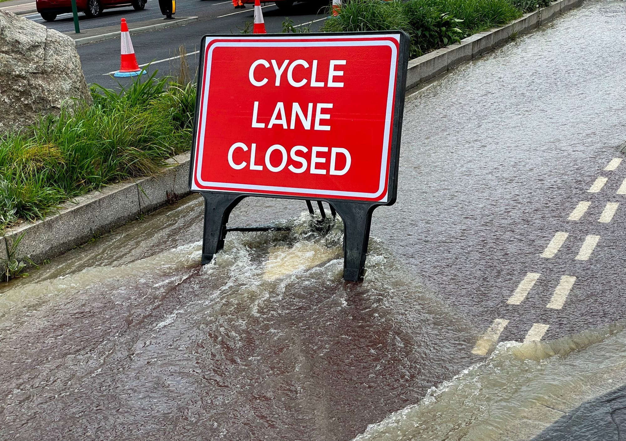 A bike lane covered in water with a red sign saying it is closed.