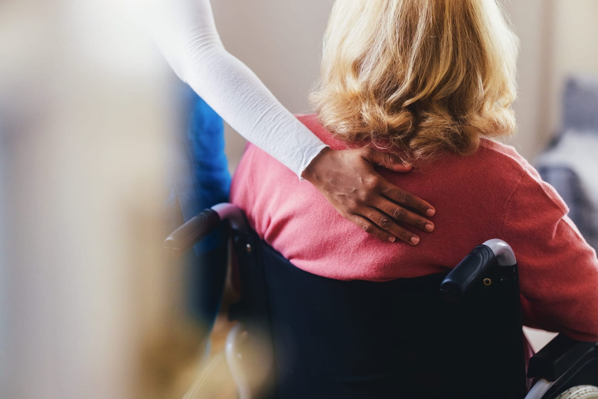 Rear view of a caregiver offering comfort and assistance to an elderly woman seated in a wheelchair. T