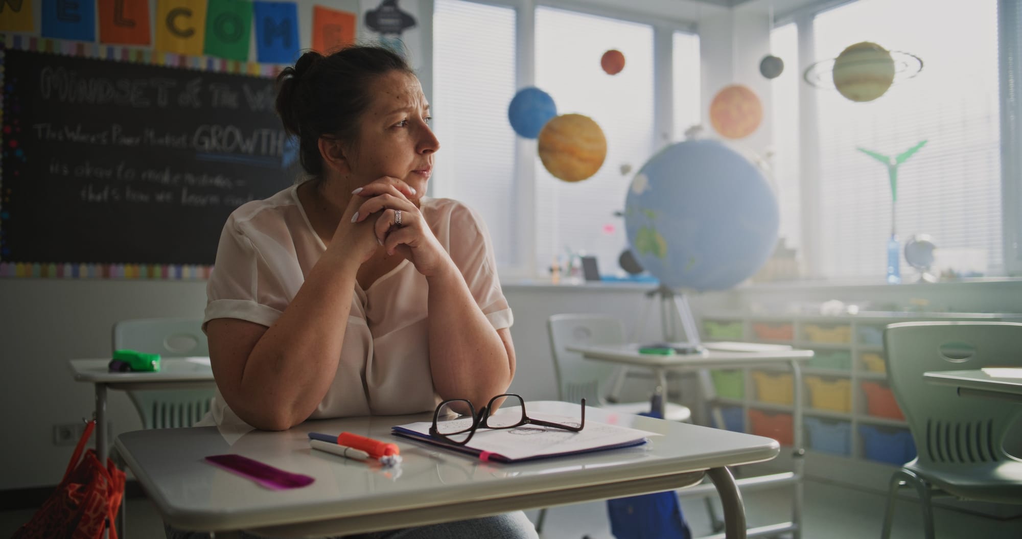Female teacher sitting alone at a desk in an empty classroom.