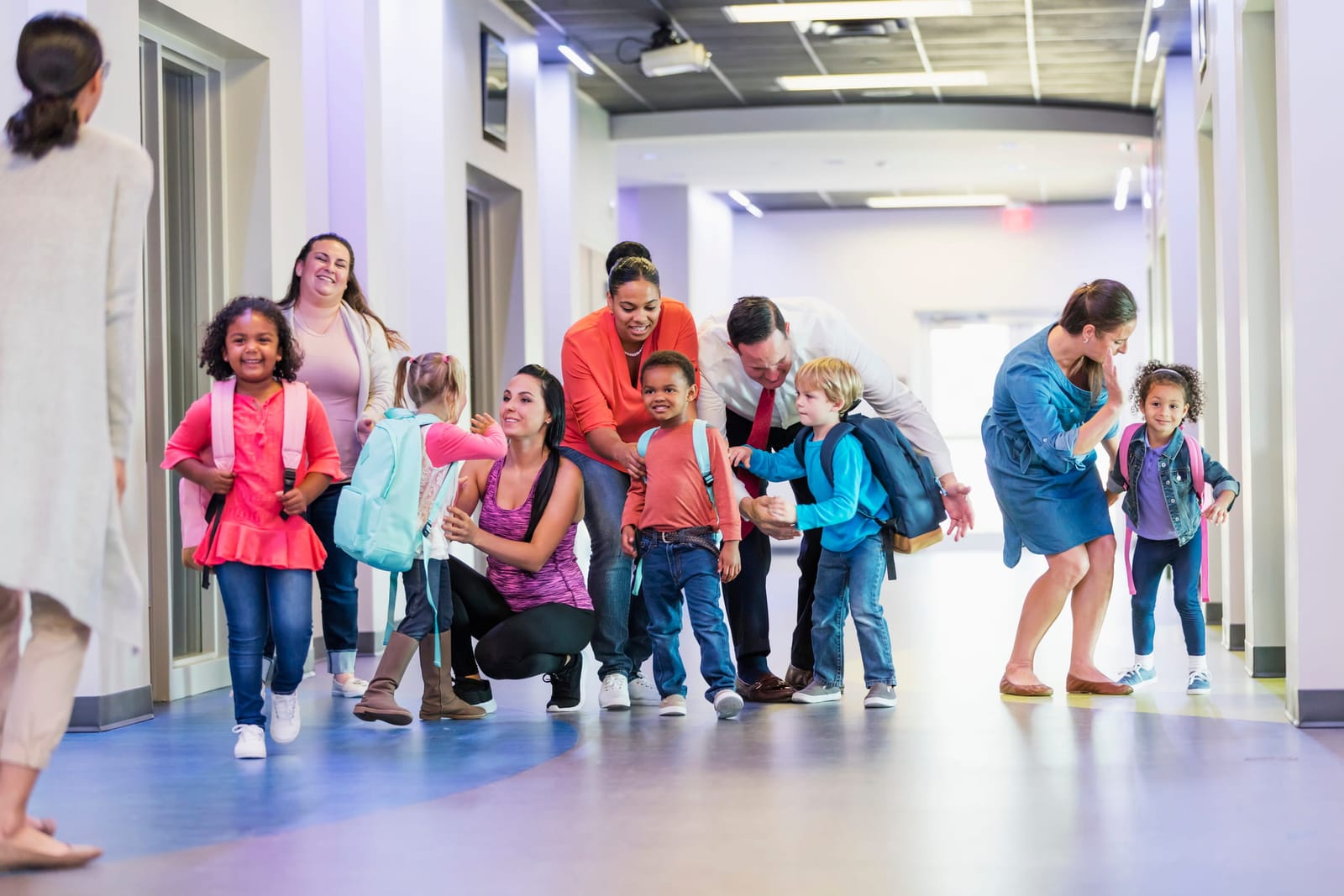 A multi-ethnic group of five preschool children, each with a parent, standing in a school hallway, getting words of encouragement.