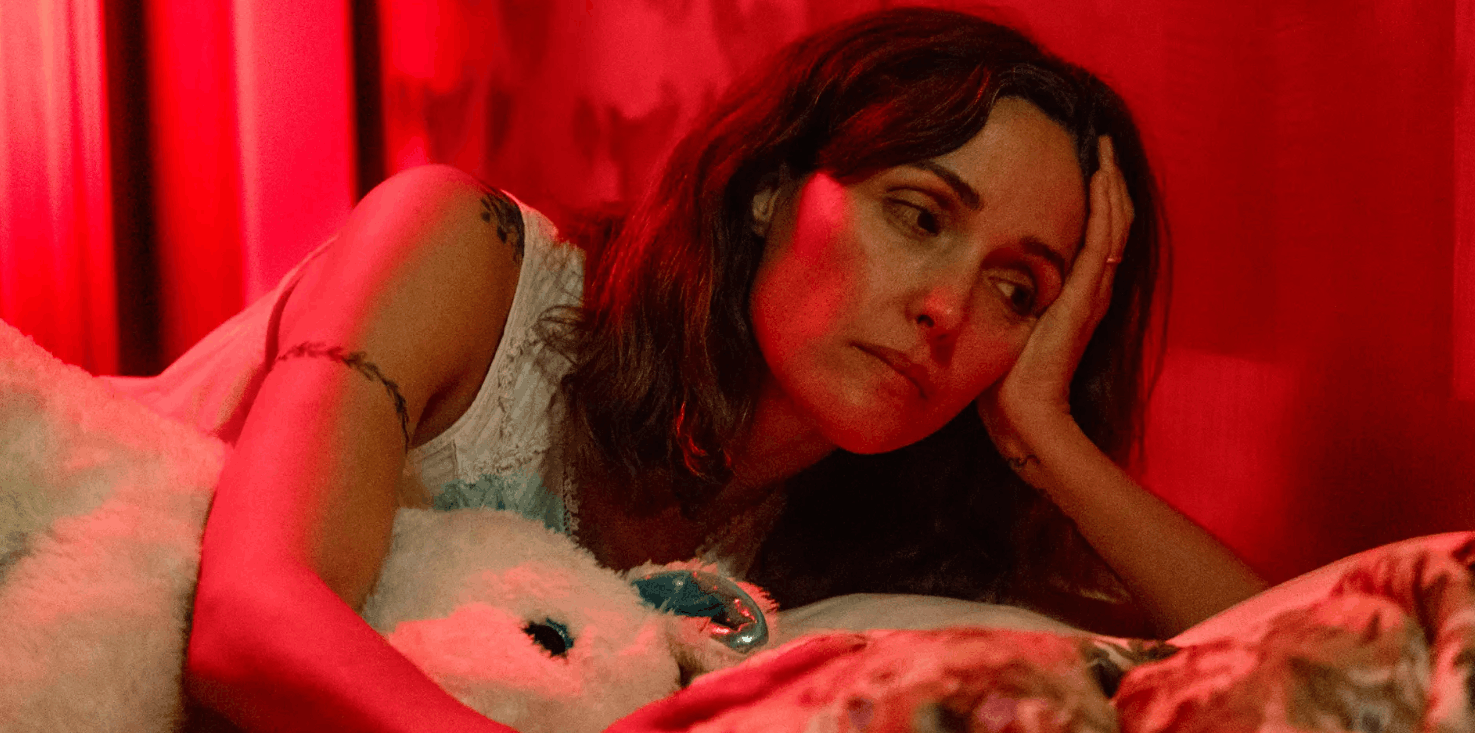 A morose Rose Byrne playing Linda laying on a bed in the film If I had Legs I'd Kick You