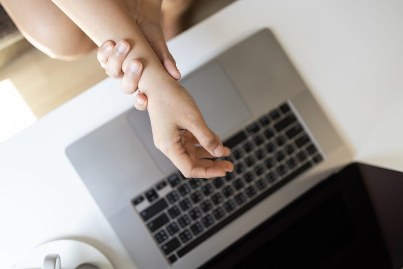 A woman clutching her wrist about a laptop keyboard