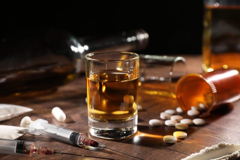 Whiskey in glass, syringes, pills and cocaine on wooden table