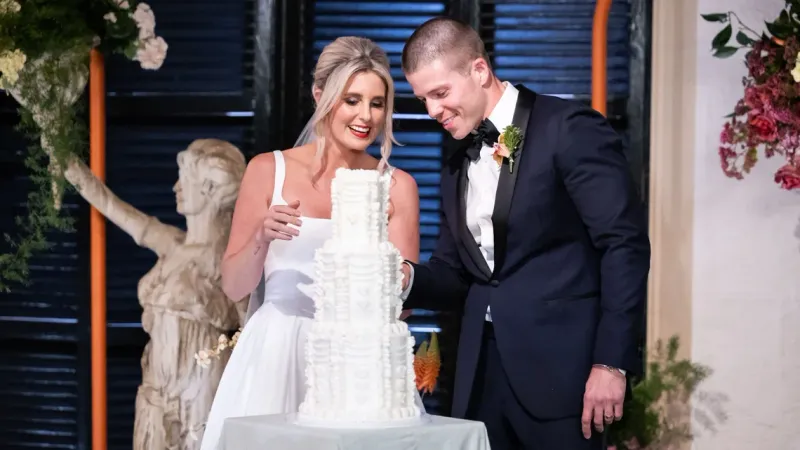 a bride and groom smiling as they look at a wedding cake