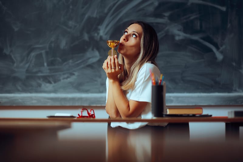 Teacher sitting at a school desk kissing a gold cup.